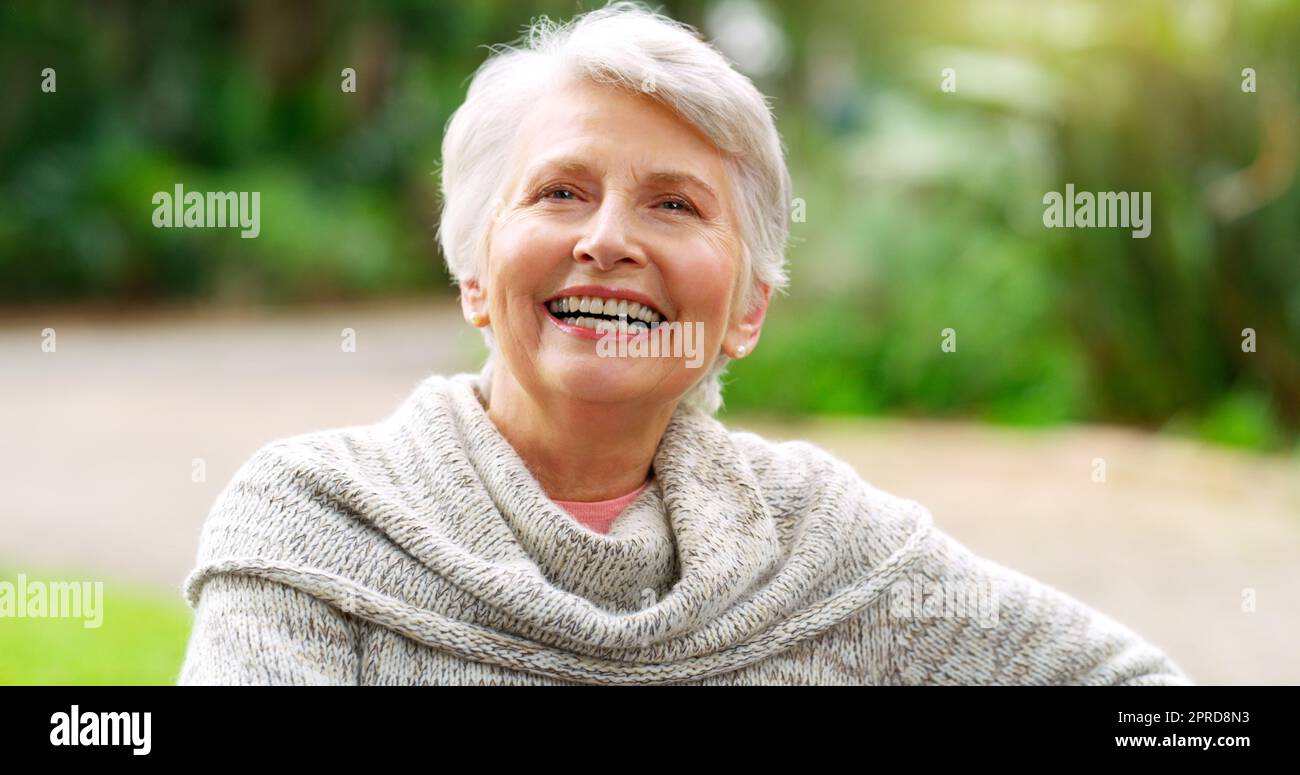 Adoro trascorrere il tempo da solo: Una donna anziana allegra seduta su una panchina esterna in un parco durante il giorno. Foto Stock