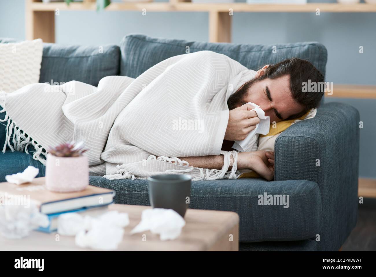 Im ammalato e divano cavalcato. Un giovane malvolo gli soffia il naso con un fazzoletto nel suo salotto. Foto Stock