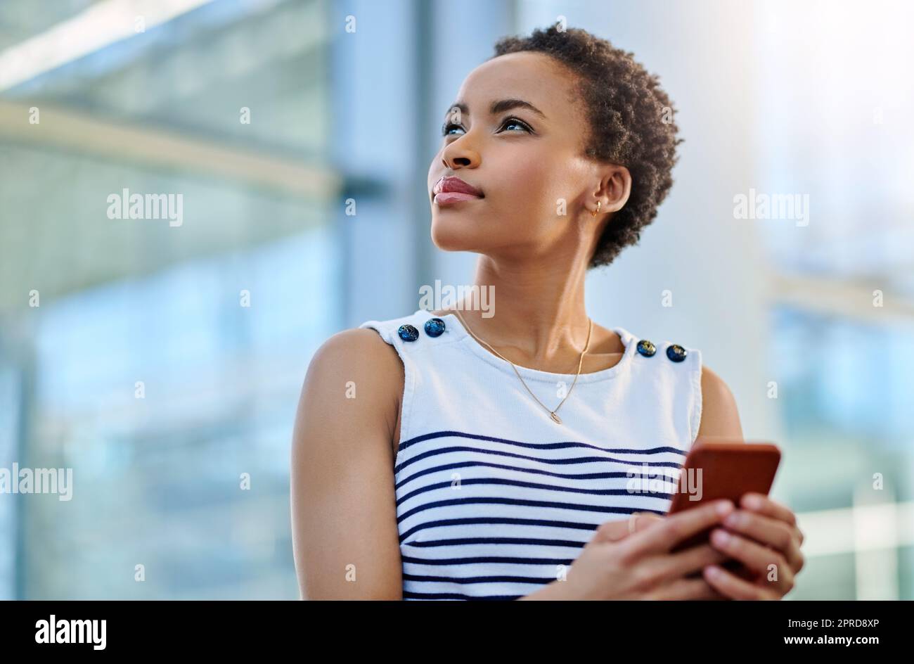 Tieni gli occhi puntati sulle stelle. Una giovane e attraente donna d'affari che guarda premurosa mentre usi uno smartphone in un ufficio moderno. Foto Stock