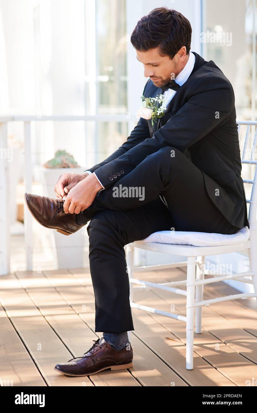 E' ora di entrare in un nuovo capitolo della mia vita. Foto a figura intera di un bellissimo giovane sposo seduto su una sedia e che si lega i lacci delle scarpe il giorno del suo matrimonio. Foto Stock