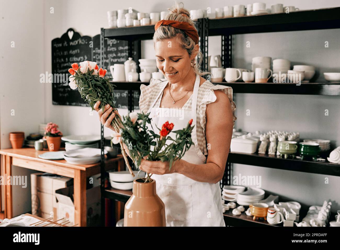 Decorando il mio studio. Una donna matura attraente in piedi da sola e mettendo i fiori in un vaso fatto a mano nel suo laboratorio di ceramica. Foto Stock