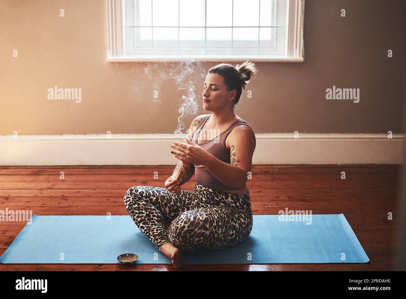Il fumo dei bastoni di palo santo è così potente che pulisce. Una giovane donna che brucia un bastone di palo santo mentre si siede su un tappeto di yoga a casa. Foto Stock