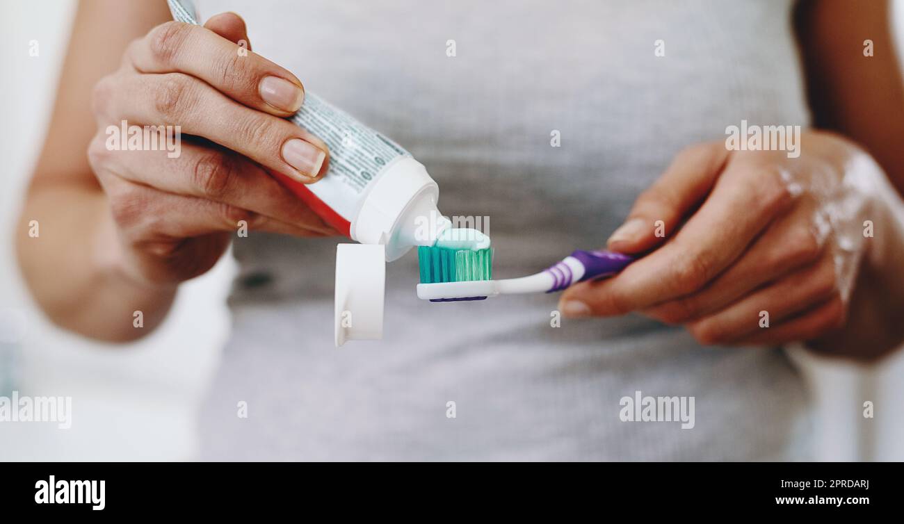 Proteggi il tuo sorriso a tutti i costi. Una donna irriconoscibile che stringe dentifricio sullo spazzolino a casa. Foto Stock