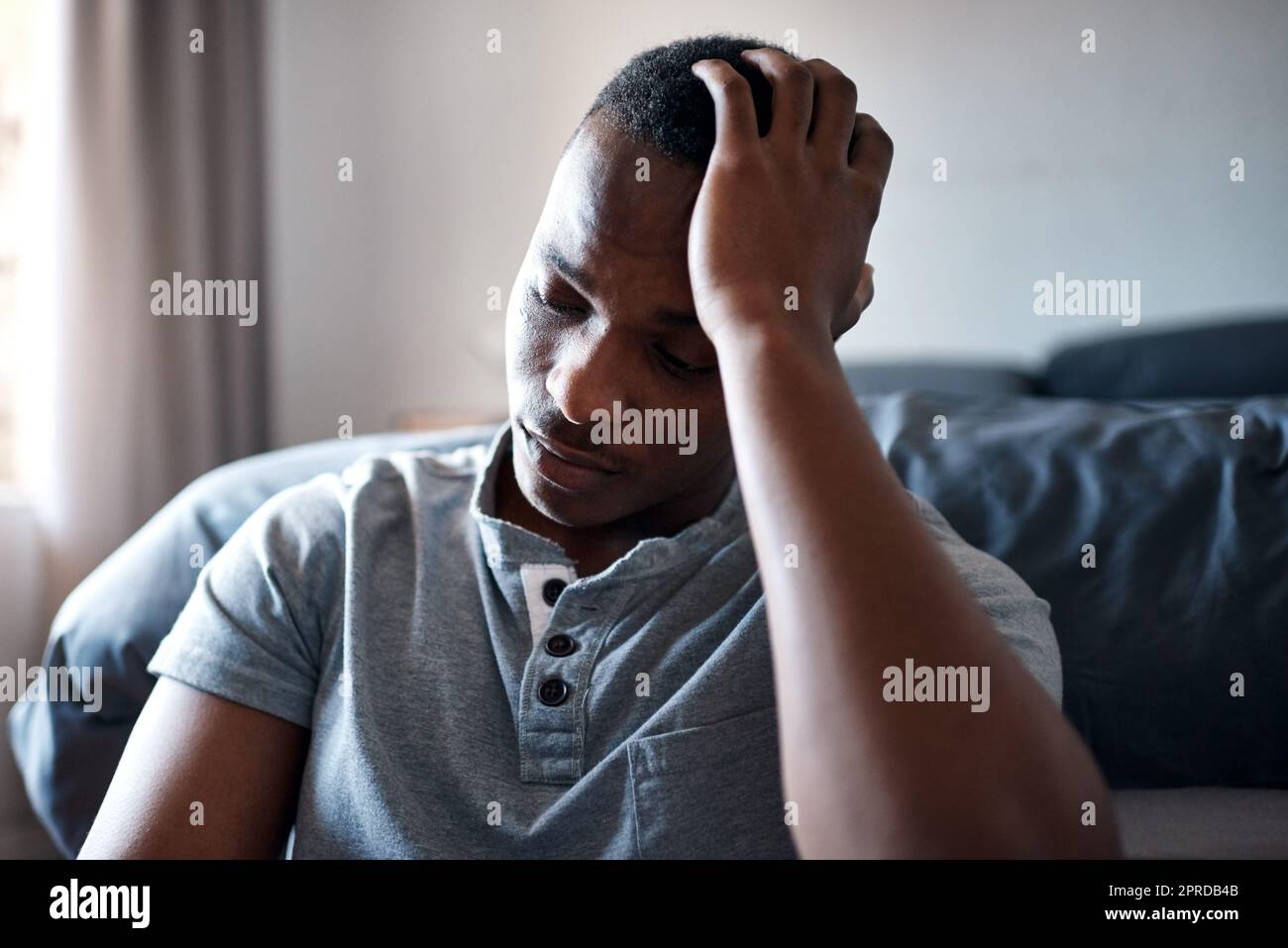 La mia testa mi fa male tanto: Un bel giovanotto seduto ai piedi del suo letto e che si sente depresso mentre era solo a casa. Foto Stock