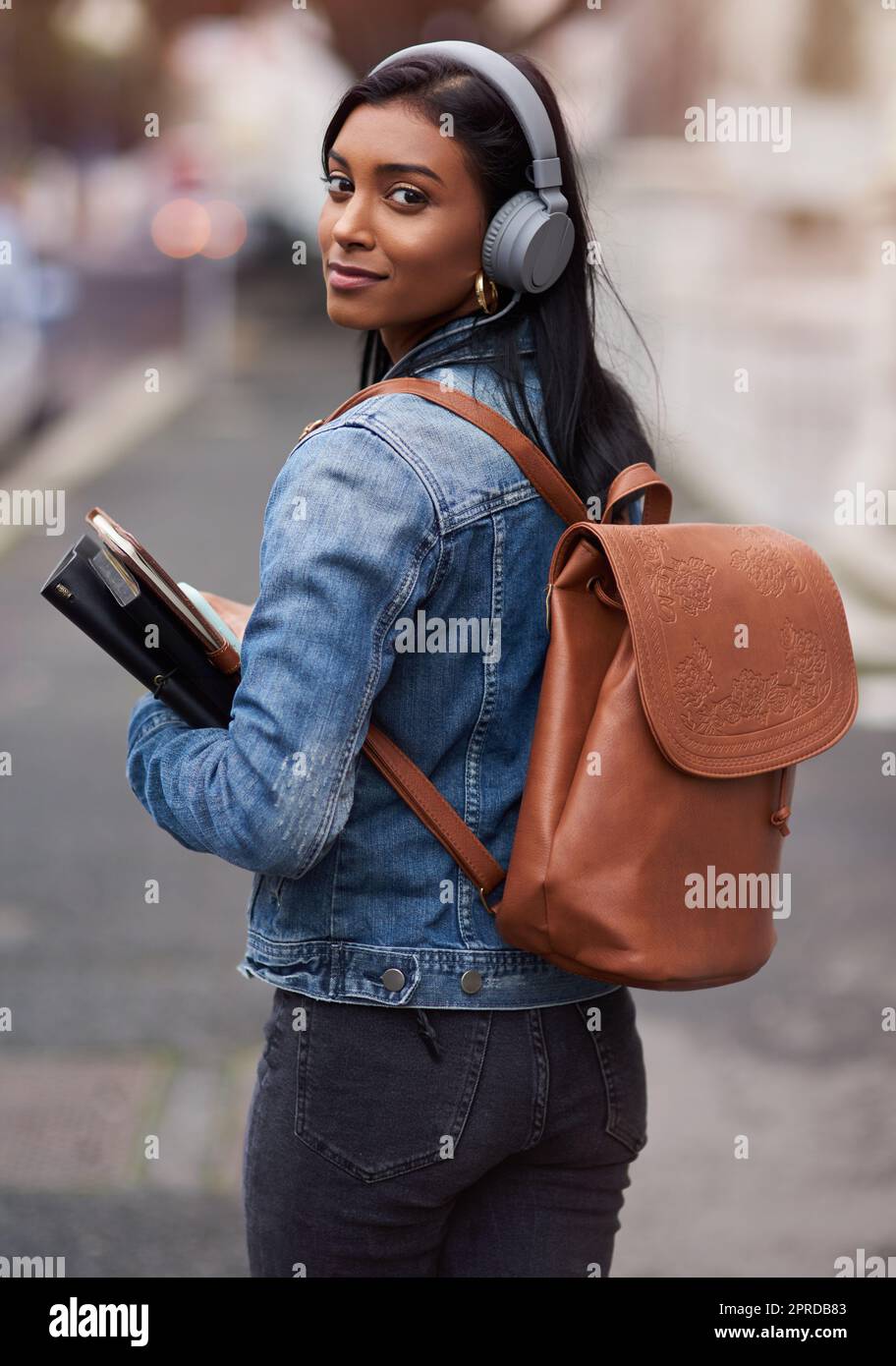 Oggi devi iniziare il tuo futuro: Una giovane donna che cammina per la città indossando le cuffie mentre trasporta i suoi libri. Foto Stock