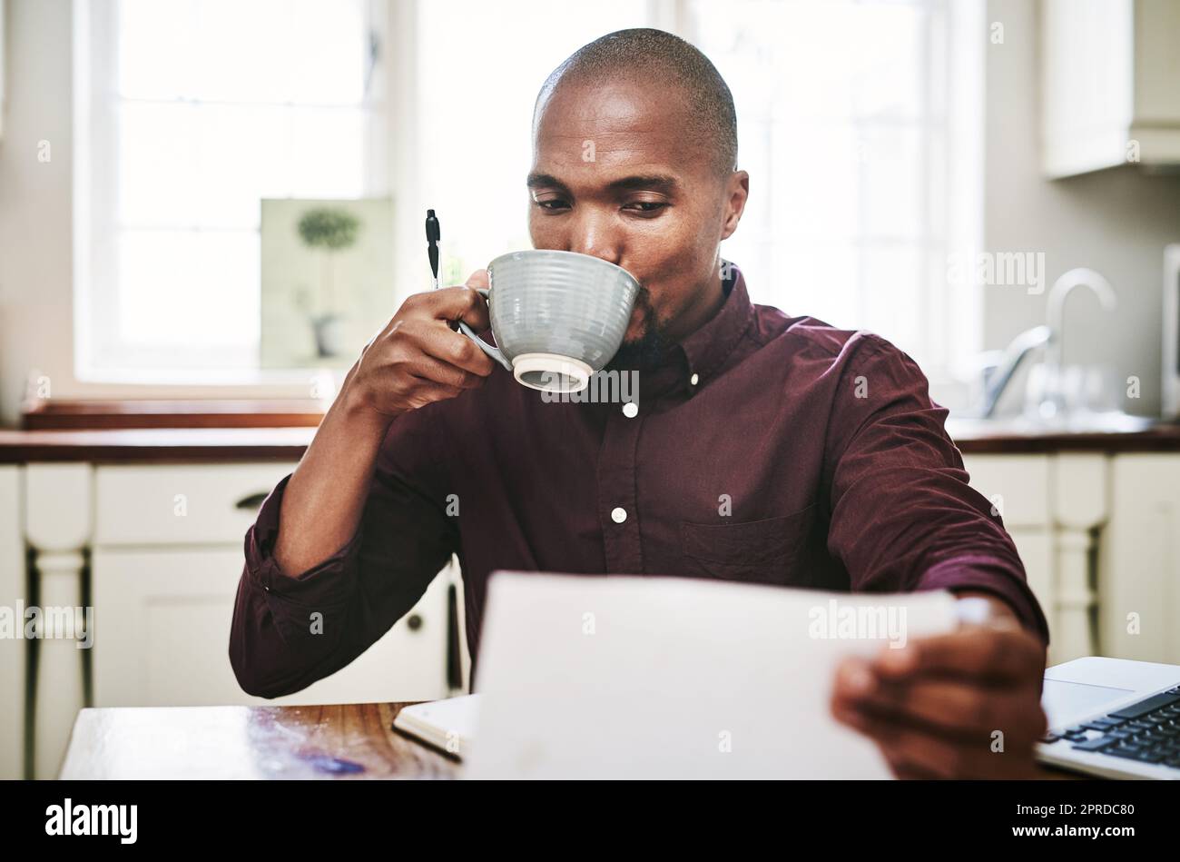 La caffeina alimenta la mia produttività. Un bel giovane uomo che beve caffè e che passa sopra il lavoro di ufficio a casa. Foto Stock