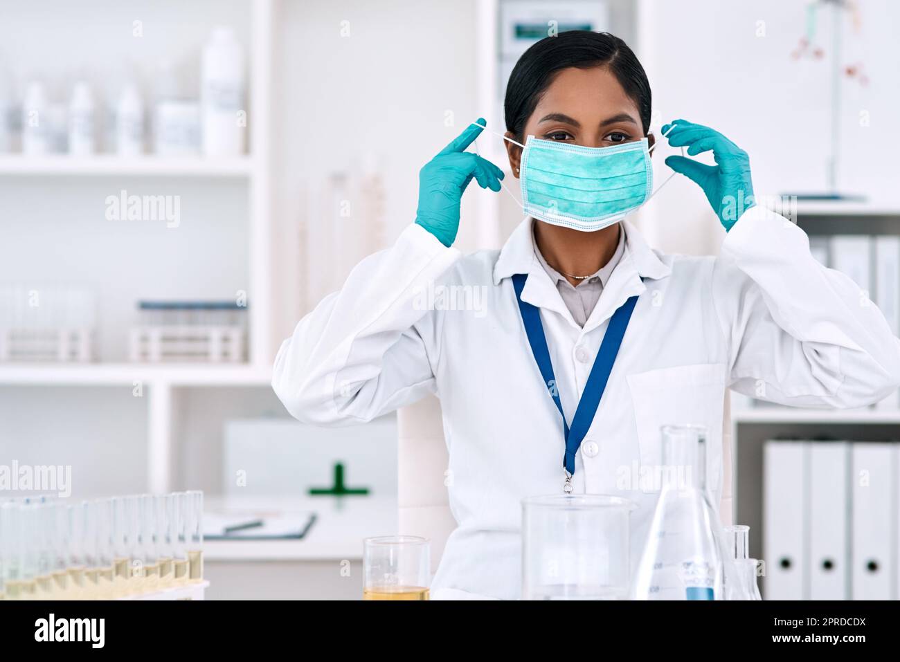 La sicurezza è una priorità di tutti gli scienziati: Una giovane scienziata attraente che si mette su una maschera mentre lavora in un laboratorio. Foto Stock