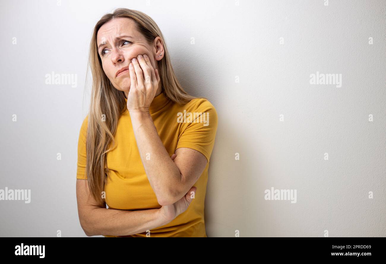 Donna di mezza età che tocca la sua guancia/bocca con espressione dolorosa a causa di problemi dentali/mal di denti Foto Stock