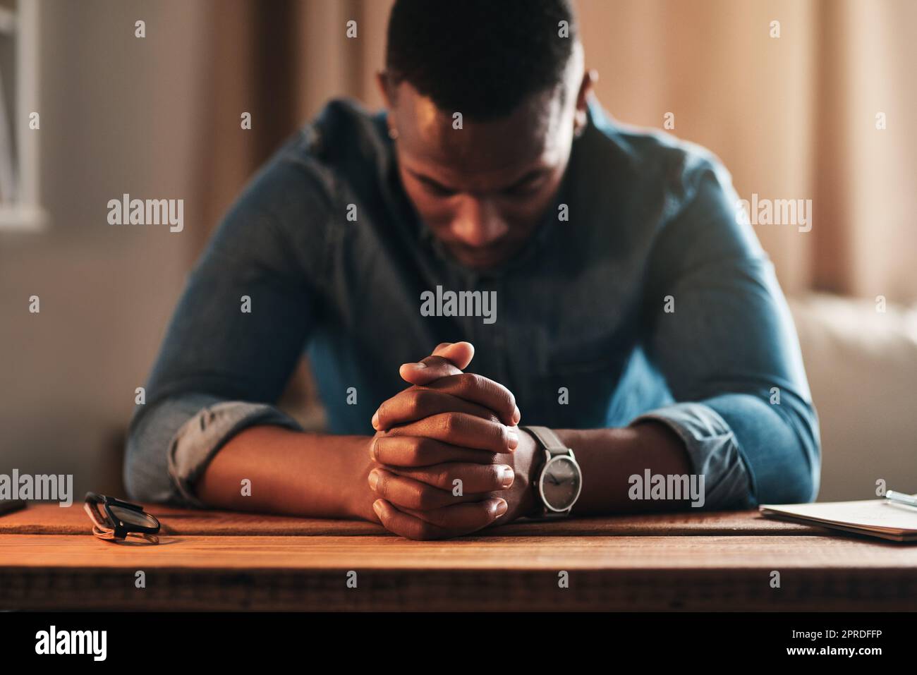 Uomo tranquillo, calmo e spirituale che prega mentre si inginocchia con le mani legate da solo a casa. Orante, spirituale e religioso, cristiano maschio che dice una preghiera quotidiana al mattino in una camera da letto Foto Stock