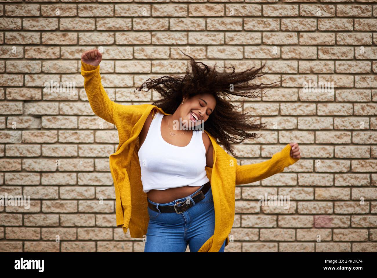Siate autentici e mostrate le vostre mosse. Una giovane donna felice che balla contro un muro di mattoni. Foto Stock