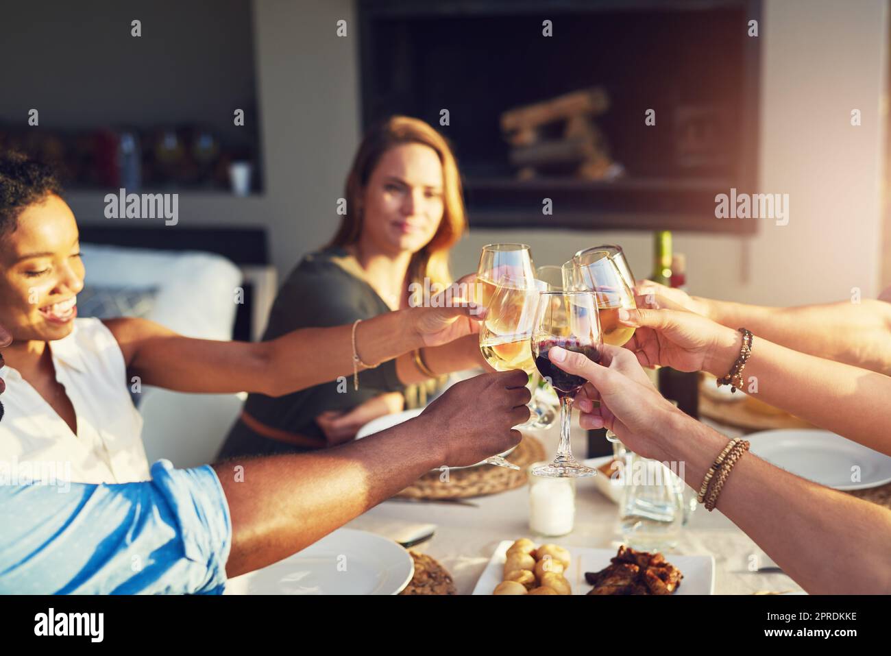 Un gruppo di amici che alzano i bicchieri per un toast mentre si siedono attorno a un tavolo insieme all'aperto, fa il tifo per molti altri anni di amicizia. Foto Stock