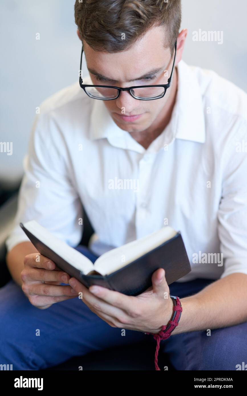 La conoscenza sarà sempre potere, un bel giovane uomo d'affari che legge la sua bibbia al lavoro. Foto Stock