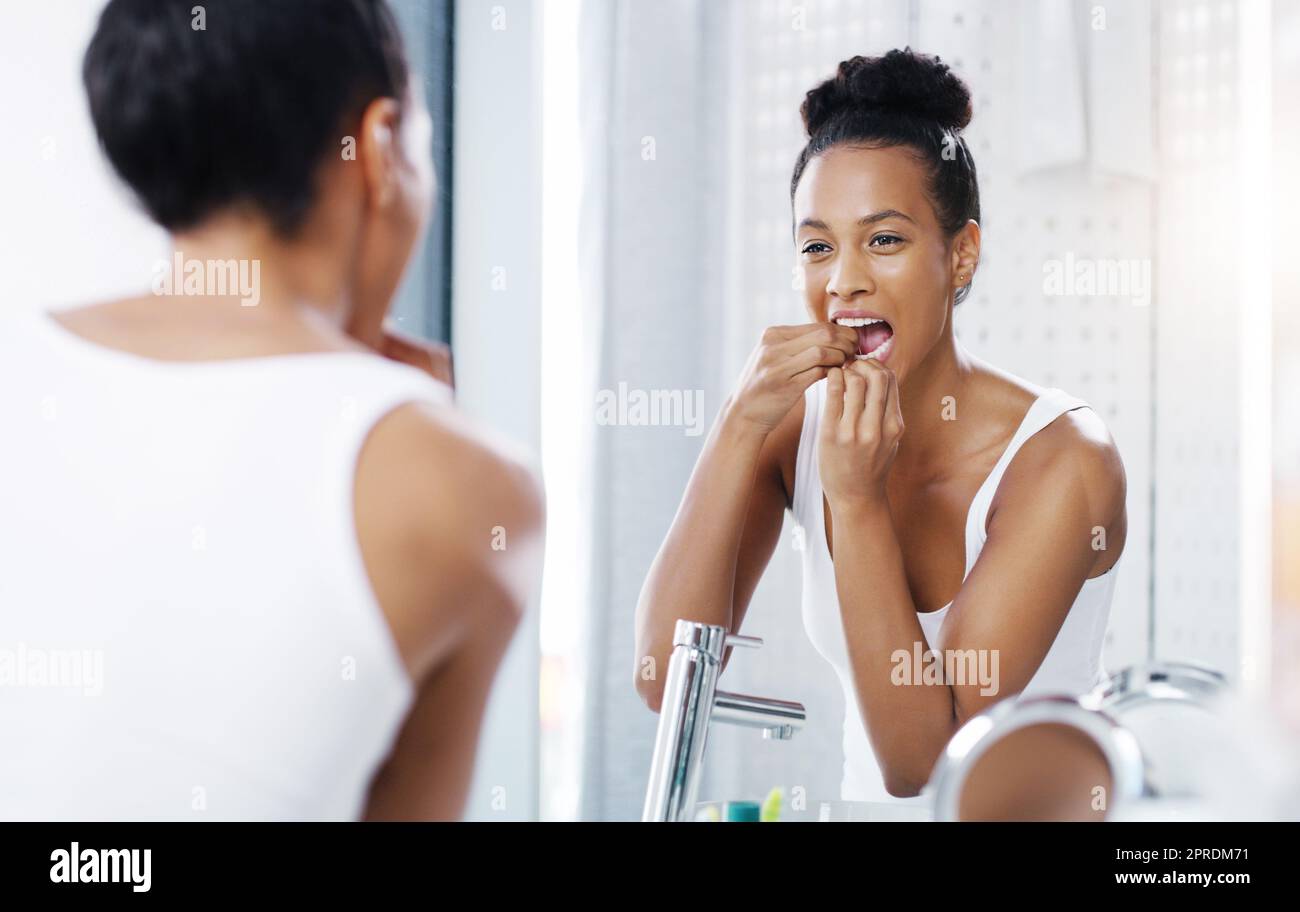 Spero che tutti si siano ricordati di far passare il filo del filo: Una giovane donna attraente che le ha fatto passare i denti mentre guardava lo specchio del bagno a casa. Foto Stock