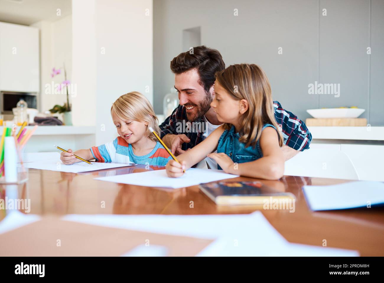 Imparare dovrebbe essere un'attività di famiglia. Un padre giovane che aiuta i suoi due bambini piccoli con i loro compiti a casa. Foto Stock