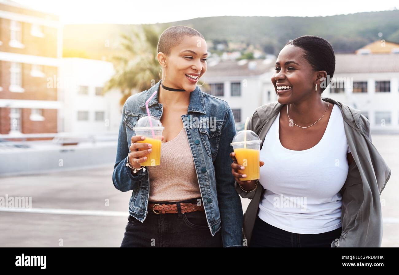 Condividere momenti con ogni sorso. Due giovani donne che camminano in città ridendo mentre tengono le loro bevande fresche. Foto Stock
