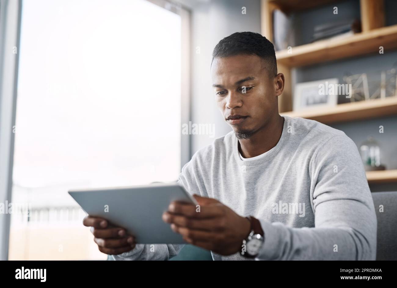 Forse dovrei solo provare questo. Un bel giovane uomo che usa il suo tablet digitale mentre si siede su un divano a casa. Foto Stock