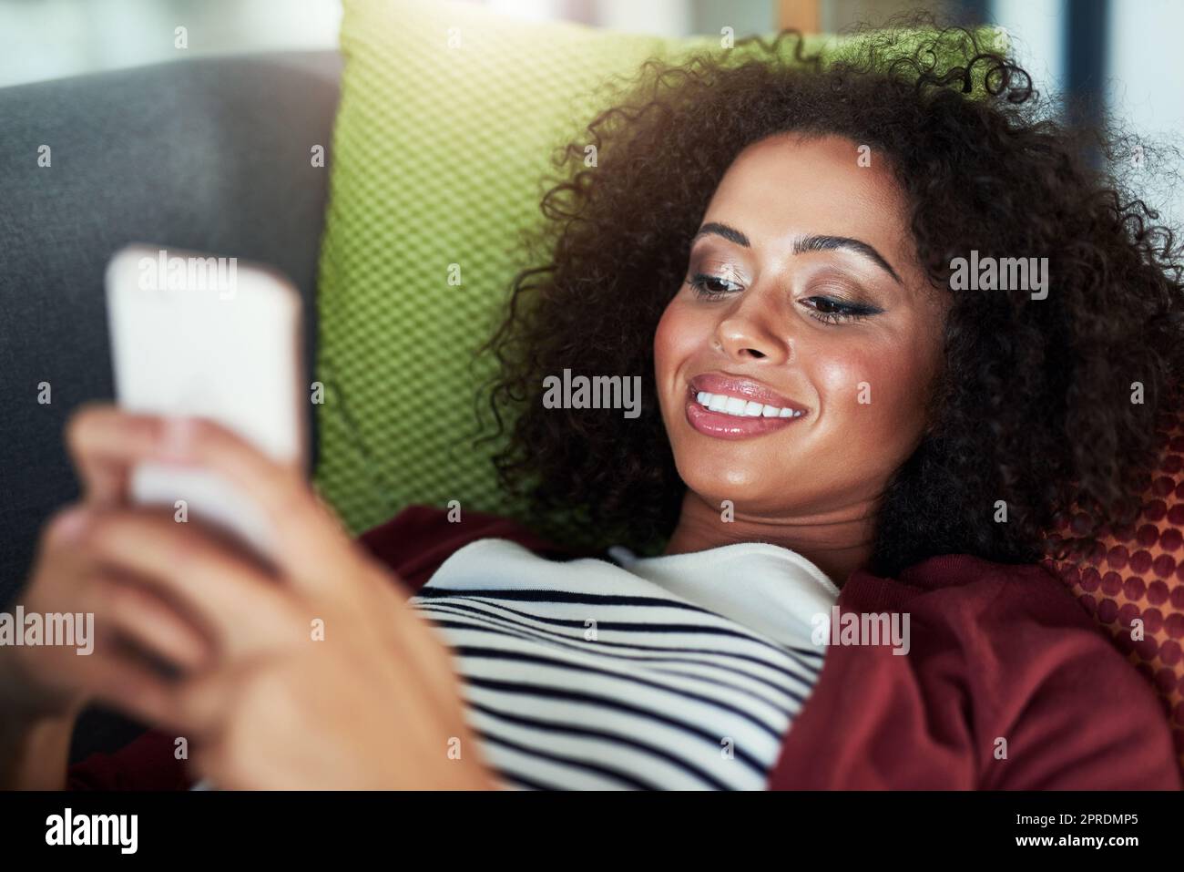 Un'altra donna che usa un telefono cellulare mentre si rilassa sul divano di casa. Foto Stock