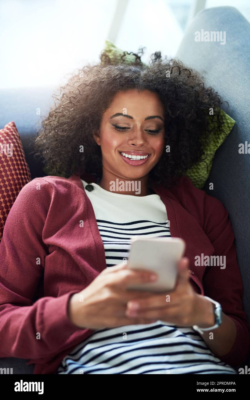 Mettetevi in contatto con una buona compagnia. Una giovane donna che usa un telefono cellulare mentre vi rilassate sul divano di casa. Foto Stock