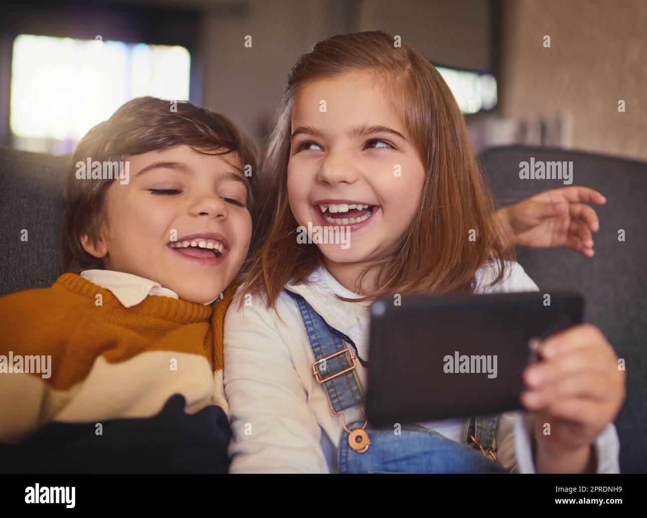 Amano scattare selfie, una bambina adorabile e suo fratello minore scattano selfie mentre si siedono sul divano di casa. Foto Stock