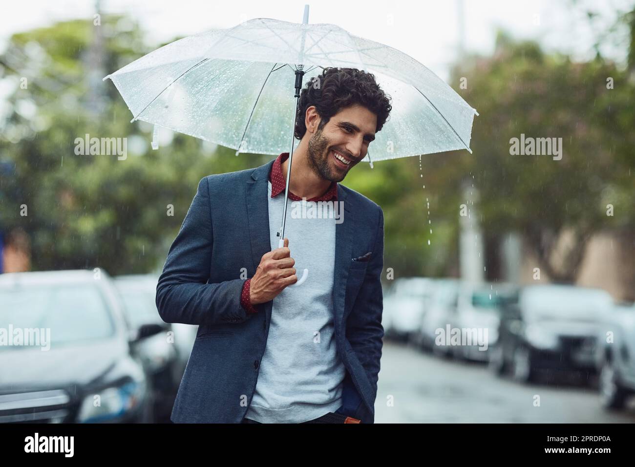 Niente può mettere a freno il suo buon umore. Un bel giovane uomo d'affari al mattino si reca sotto la pioggia. Foto Stock