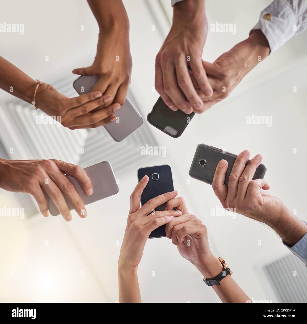 Il team che rimane connesso. Inquadratura ad angolo basso di un gruppo di colleghi che utilizzano i loro smartphone in sincronia. Foto Stock