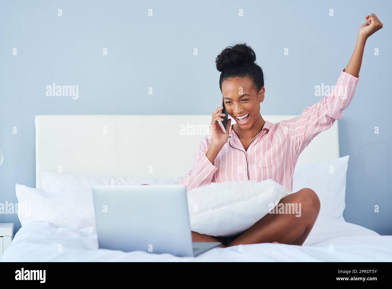 Spero che non sia troppo presto per iniziare a festeggiare: Una giovane donna attraente che prende una telefonata mentre usa il suo portatile a letto a casa. Foto Stock