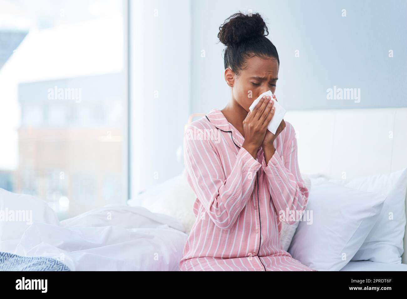 Non è il miglior inizio della mia mattina, una giovane donna malata che soffia il naso con un fazzoletto nella sua camera da letto a casa. Foto Stock