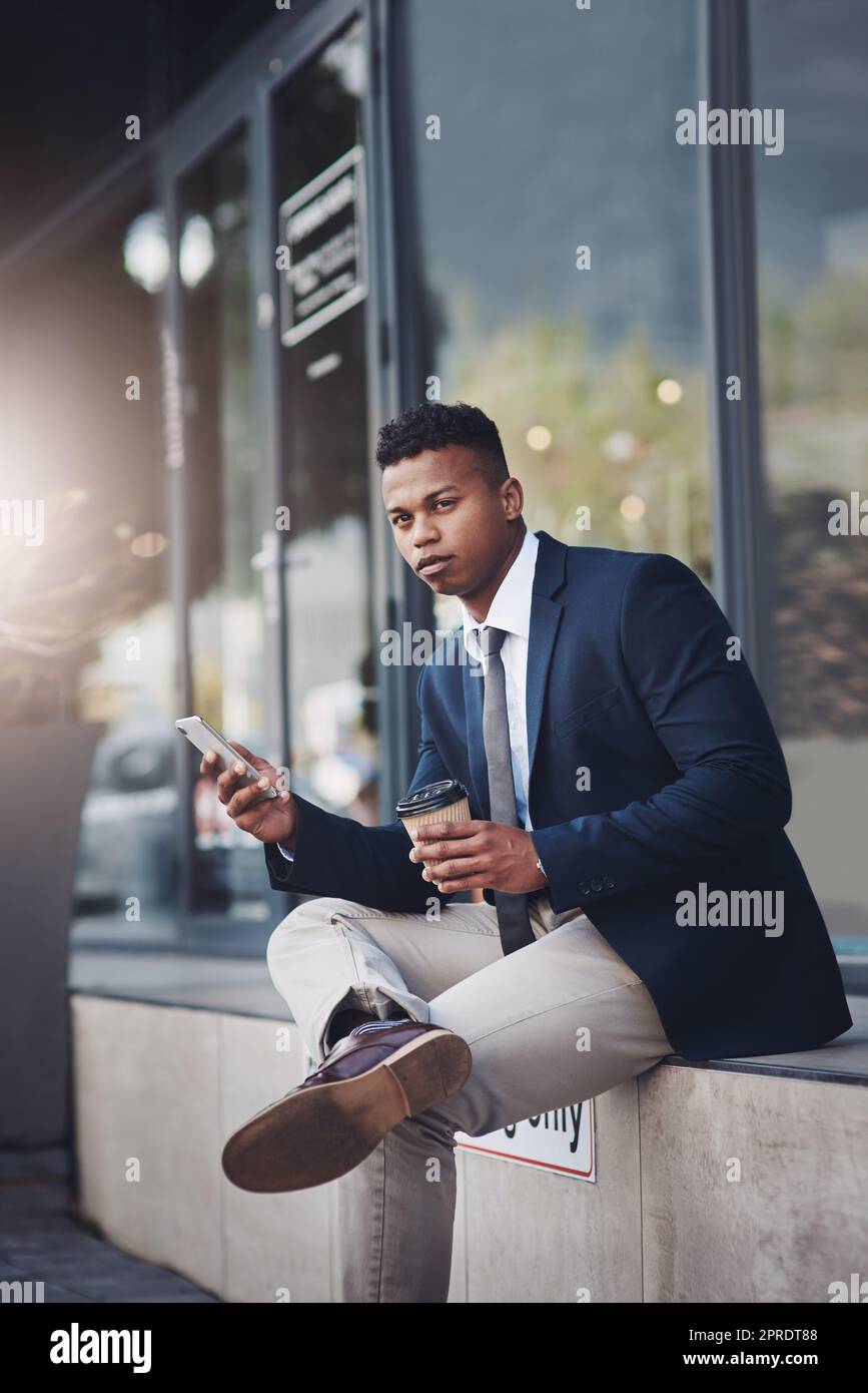 Un bel giovane uomo d'affari che usa un cellulare mentre beve un caffè in città. Foto Stock