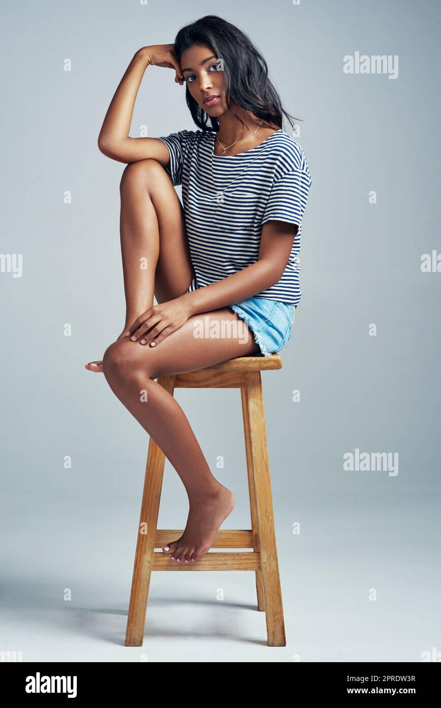 La cosa più bella è essere voi stessi. Una bella giovane donna seduta su uno sgabello di legno su uno sfondo grigio. Foto Stock