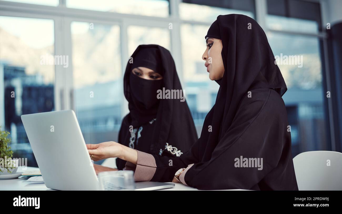 Contribuire al successo della loro azienda. Due giovani donne arabe d'affari che lavorano su un portatile nel loro ufficio. Foto Stock