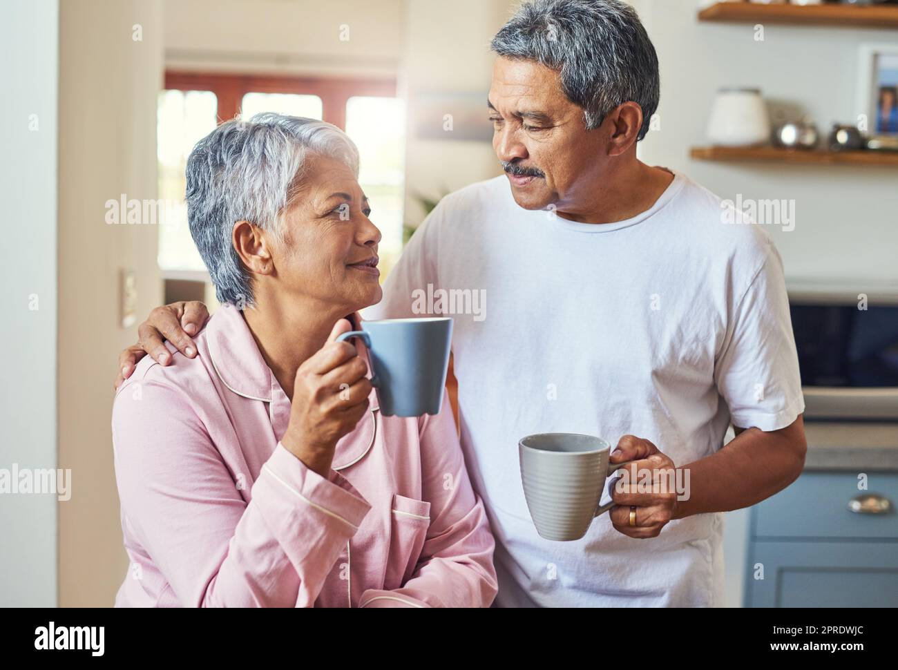 E' cosi' che cominciamo le nostre mattine. una coppia di anziani allegri che si tengono a vicenda mentre si guardano negli occhi e bevono caffè a casa durante il giorno. Foto Stock