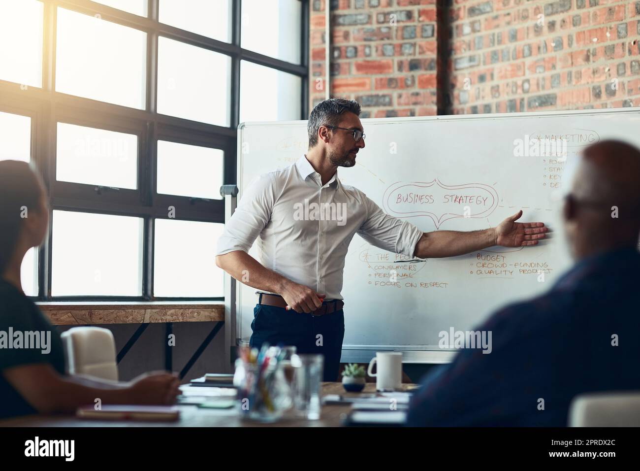 Guarda qui. Uomo d'affari che fa una presentazione in una riunione pianificando la strategia di crescita aziendale in un ufficio. Serio imprenditore maschile che informa il suo team sulla missione e la visione di avvio. Foto Stock