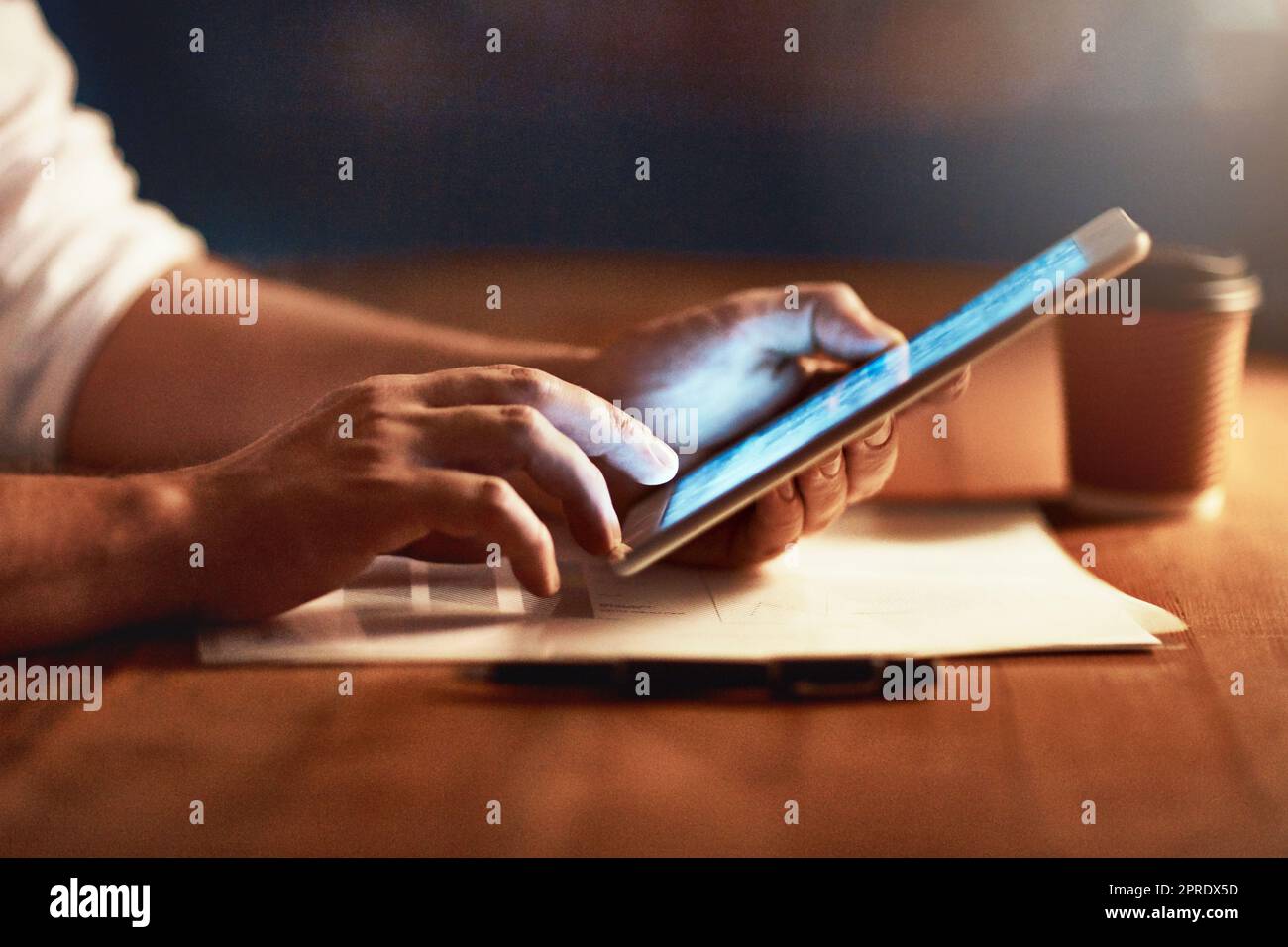 Primo piano di una persona che tiene le mani e scorre su un tablet digitale pianificando a tarda sera. Uomo moderno che lavora online con un dispositivo di visualizzazione touchscreen, alla scrivania del luogo di lavoro Foto Stock