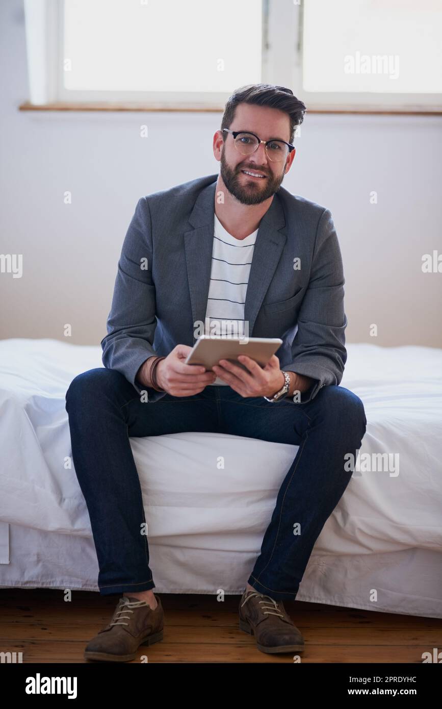 Non c'e' bisogno di uscire dalla mia zona di comfort. Ritratto completo di un bel giovane uomo d'affari che lavora su un tablet mentre è seduto sul letto a casa. Foto Stock