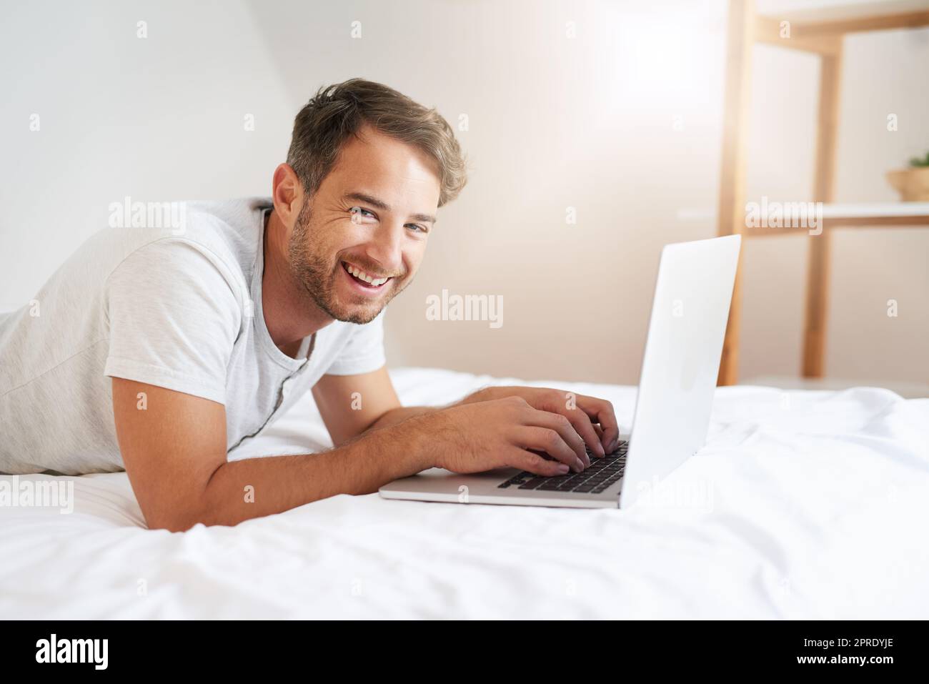 Svegliarsi con il mondo alle mie dita. Un giovane uomo che usa un computer portatile sul suo letto a casa. Foto Stock