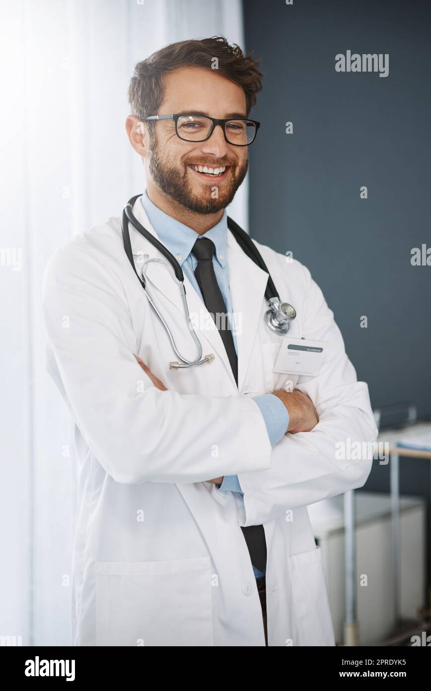 Fidatevi di me con il vostro benessere. Ritratto corto di un giovane medico fiducioso in piedi con le braccia ripiegate all'interno di un ospedale. Foto Stock
