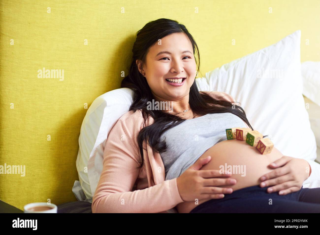 La maternità è una benedizione così bella. Ritratto di una donna incinta sdraiata con i blocchi di legno del bambino sulla sua pancia a casa. Foto Stock