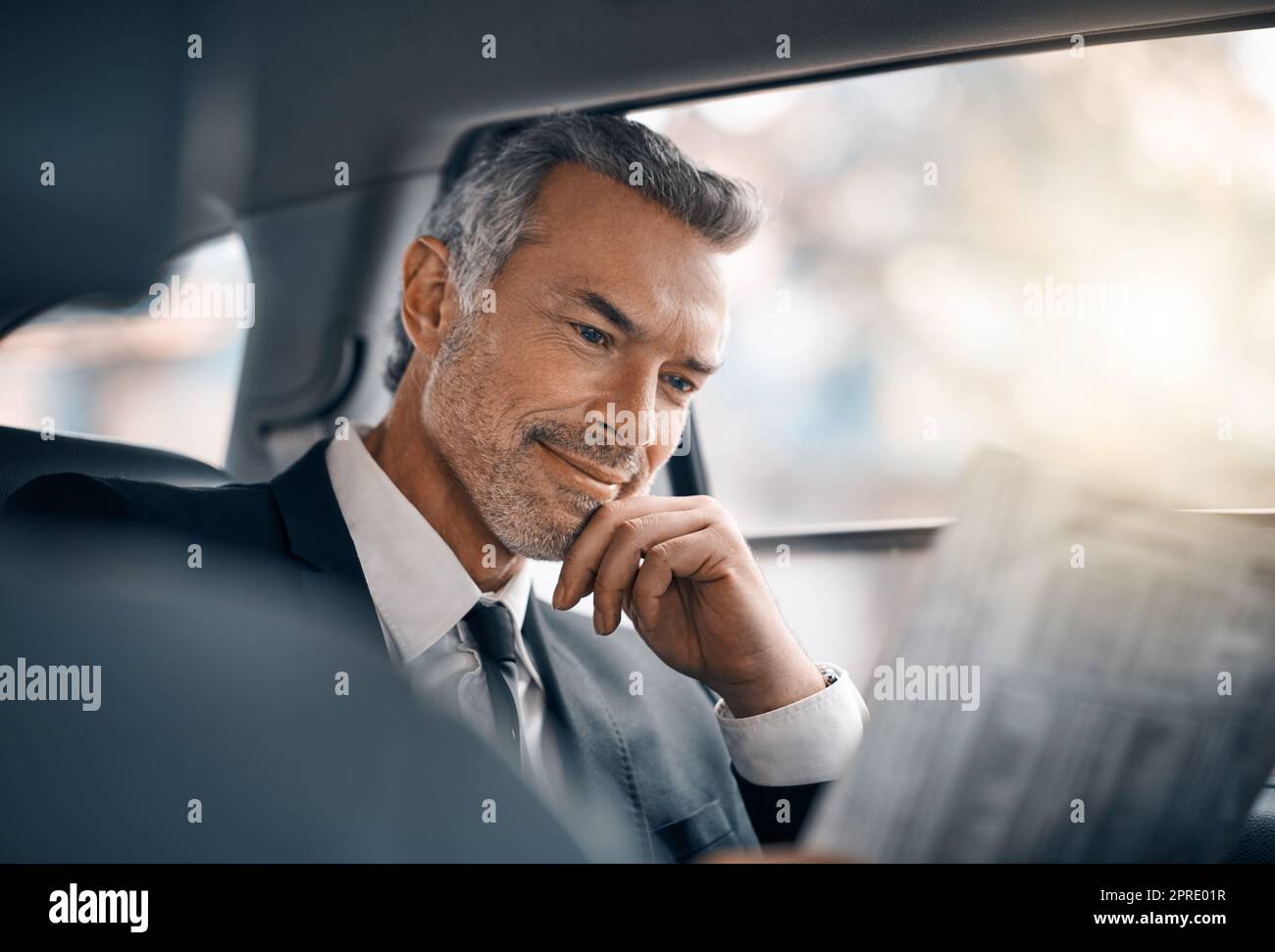 La notizia sembra buona oggi. Un bel uomo d'affari maturo che legge il giornale mentre si siede sul retro di un'auto durante il suo viaggio mattutino. Foto Stock