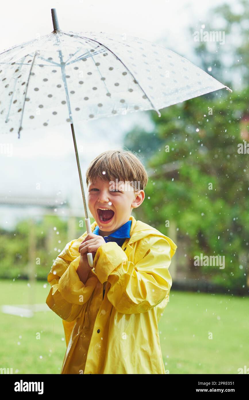 La pioggia lo rende così felice. Ritratto di un allegro ragazzino in piedi con un ombrello all'esterno in una giornata di pioggia. Foto Stock