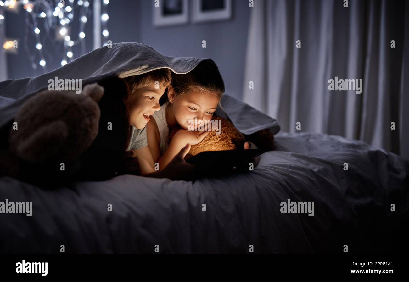 La tecnologia è solo una parte della loro educazione: Due adorabili fratelli e sorelle che usano un tablet digitale insieme a letto di notte. Foto Stock