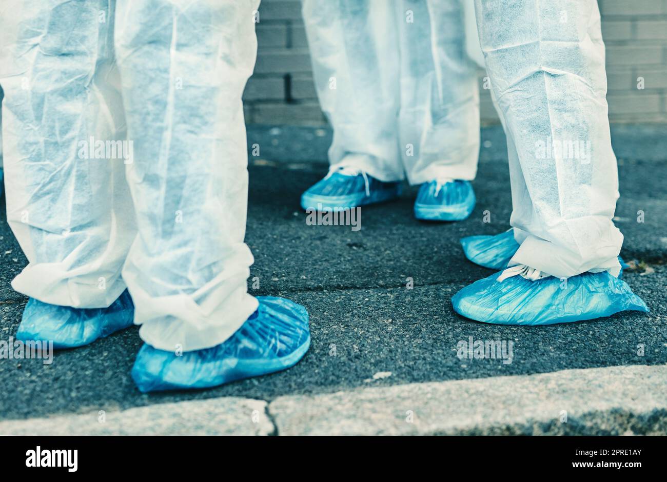 Gambe e piedi degli operatori sanitari che indossano indumenti protettivi o tute in materiale antipolvere all'aperto durante la pulizia. Primo piano di una squadra di professionisti medici che si riunisce durante la pandemia di covid o coronavirus Foto Stock