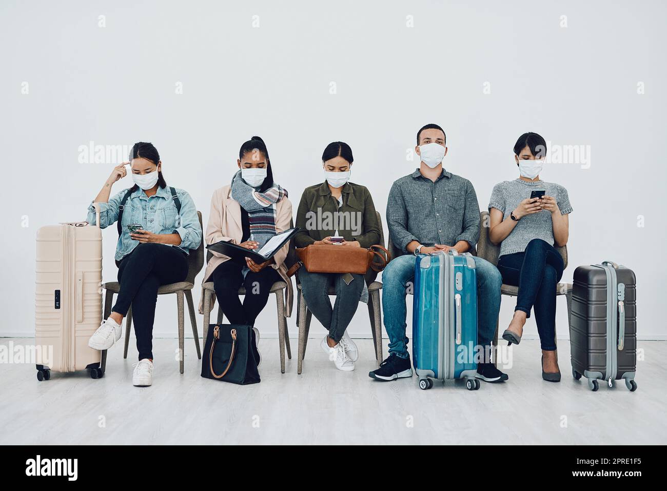 Viaggi e turismo durante la pandemia con passeggeri che indossano maschere e sono al sicuro in fila d'attesa per l'aeroporto. Gruppo di persone in una sala di partenza, pronti a salire a bordo e conformi al protocollo covid Foto Stock