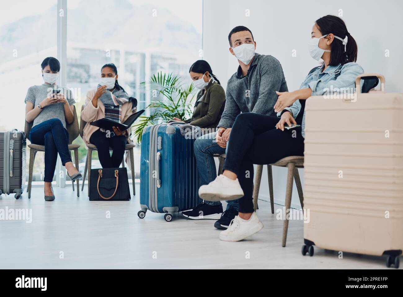 Gruppo di persone che viaggiano durante il covid in attesa in fila presso una lounge dell'aeroporto con maschere protettive. Turisti seduti in coda in una struttura di trasporto pubblico durante la pandemia di coronavirus Foto Stock