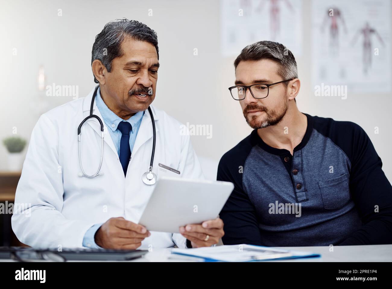 Diamo un'occhiata alla diagnostica. Un medico di sesso maschile fidato seduto alla sua scrivania mentre si consulta un paziente all'interno di un ospedale durante il giorno. Foto Stock