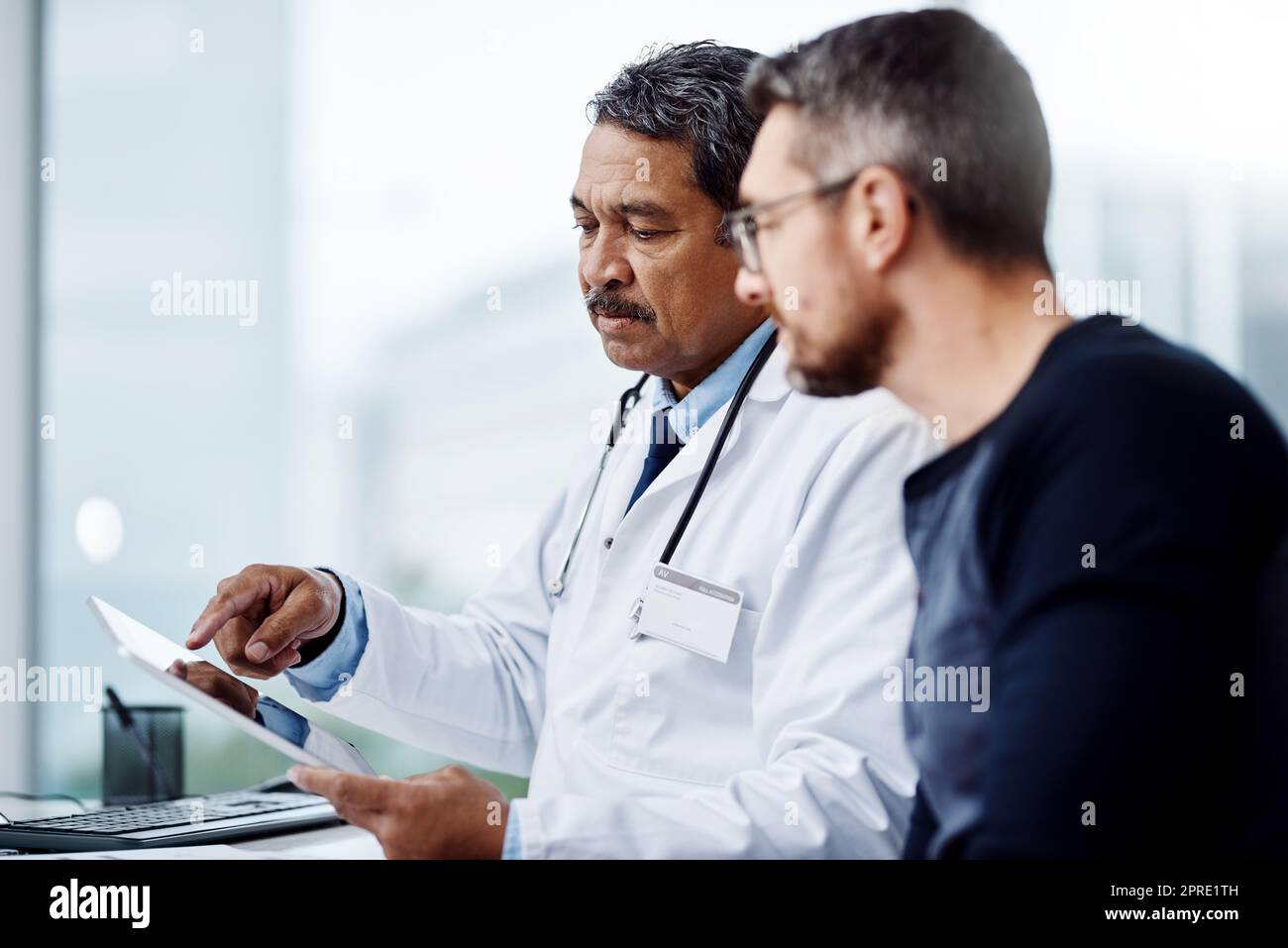 Vedete, questo è quello che mi dicono i miei rapporti. un medico maschio maturo sicuro di sé seduto alla sua scrivania mentre consultava un paziente all'interno di un ospedale durante il giorno. Foto Stock