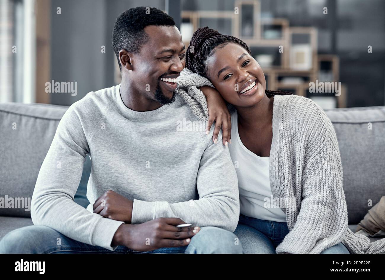 Coppia felice, innamorata e spensierata che si rilassa, sorride e ride insieme al ritratto di casa mentre si gode il fine settimana trascorso in casa. Giovane moglie africana e marito amorevole che legano sul loro divano Foto Stock