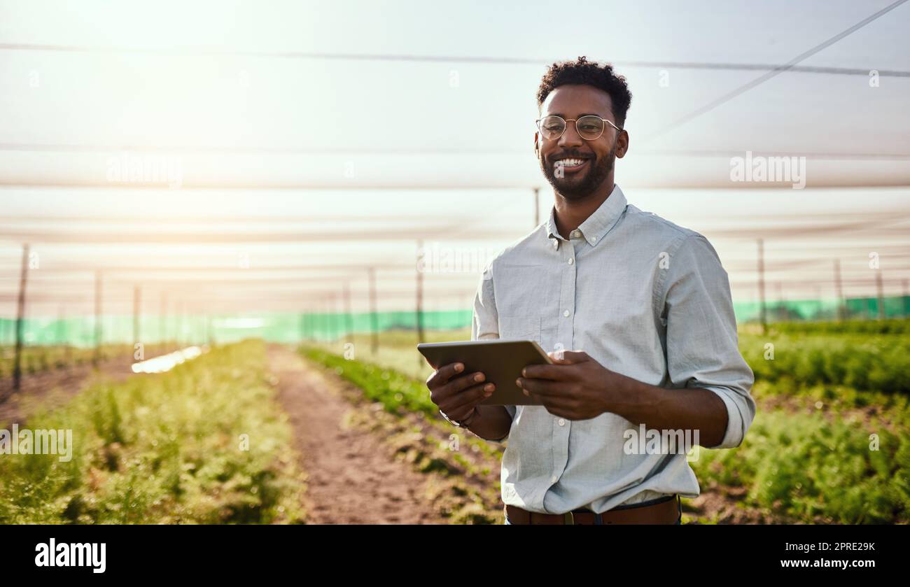 Giovane agricoltore africano che lavora su una strategia di sviluppo agricolo sano sul suo tablet digitale. Lavoratore sul campo sorridente all'aperto per l'agricoltura biologica e la sostenibilità della crescita Foto Stock