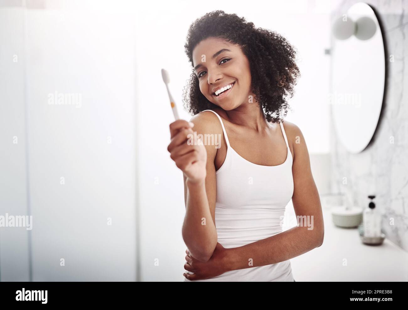 Il tuo sorriso è la curva che fissa tutto dritto. Ritratto di una giovane donna attraente spazzolando i denti nel bagno a casa. Foto Stock