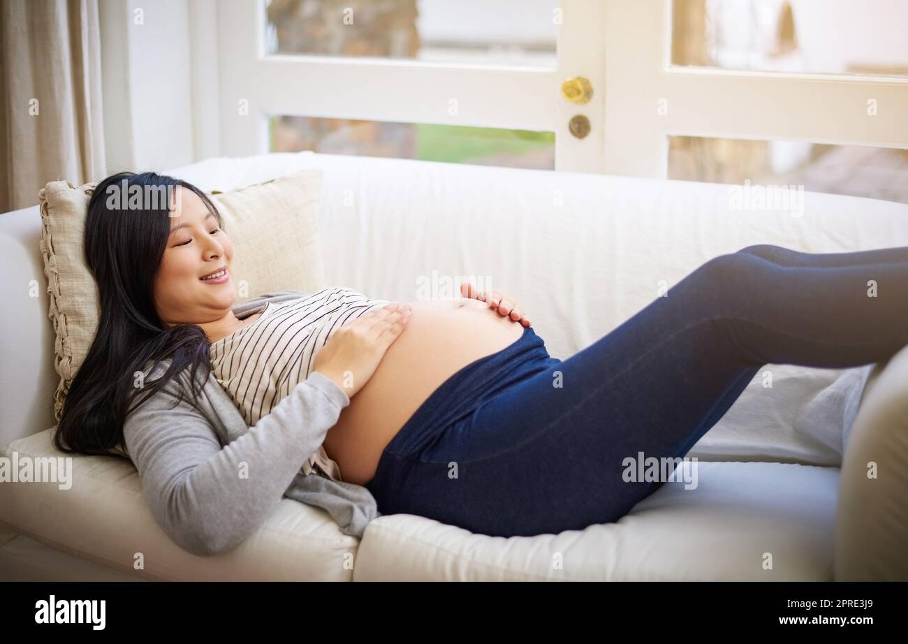 Non vedo l'ora di tenerti tra le braccia: Una giovane donna incinta allettante che si rilassa sul divano di casa. Foto Stock