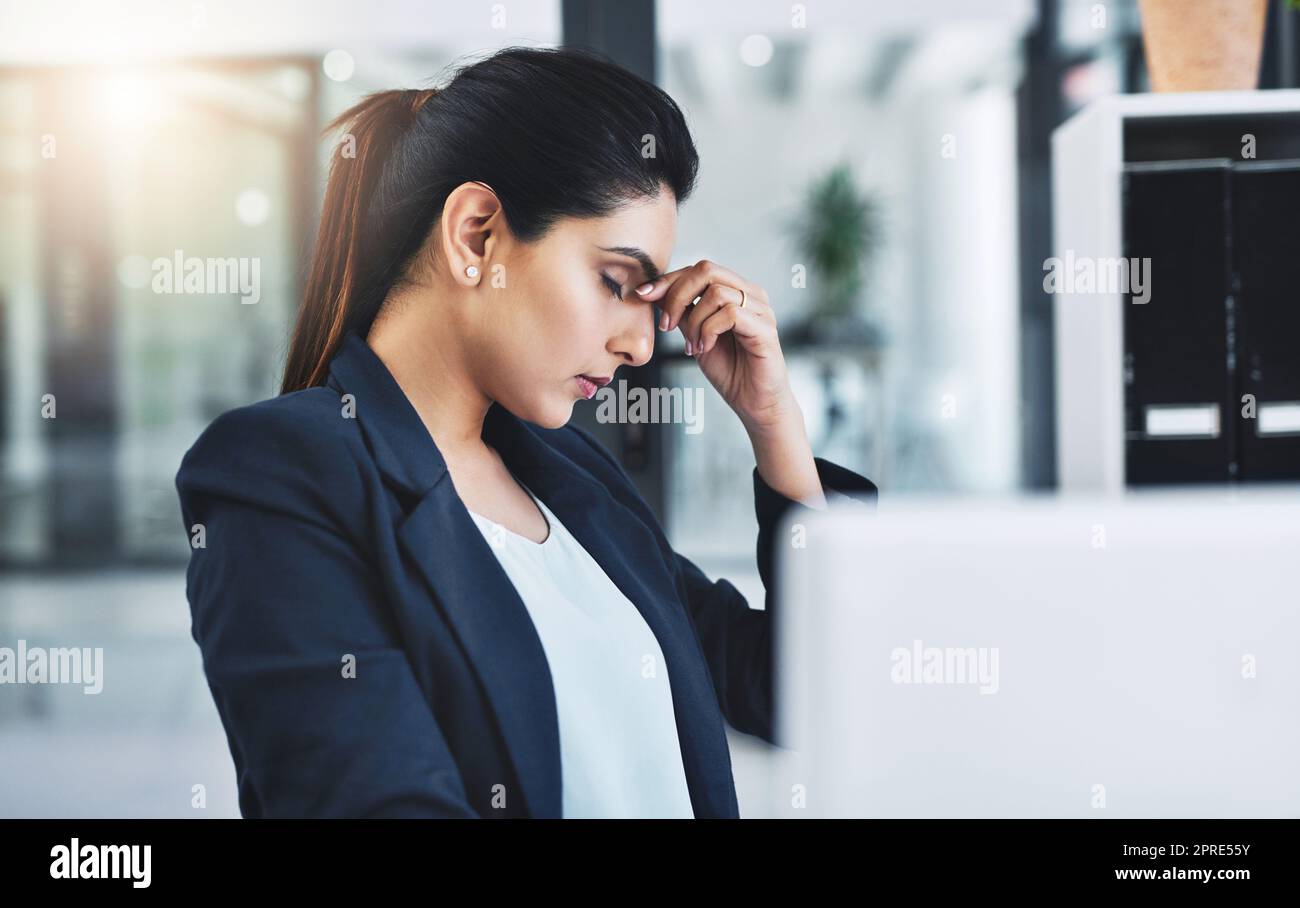 L'emicrania sul lavoro può tenervi indietro. Una giovane donna d'affari attraente che sperimenta un mal di testa nel suo ufficio. Foto Stock